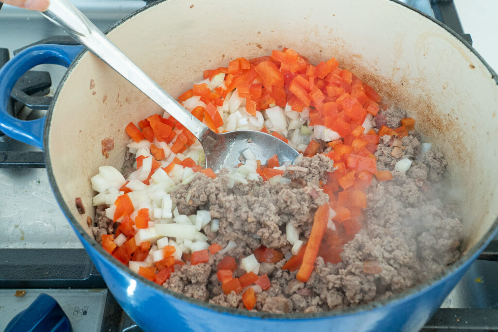 Adding red peppers and onions to meat in chili recipe