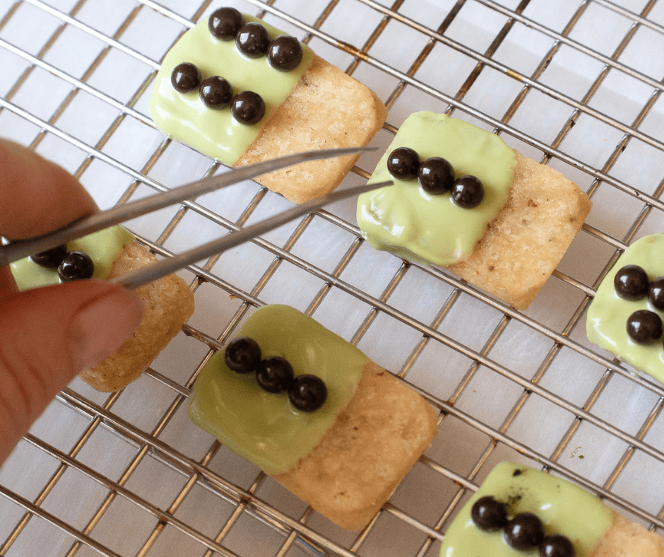 Hand with a culinary tweezer adding dark chocolate pearls to drying chocolate. 