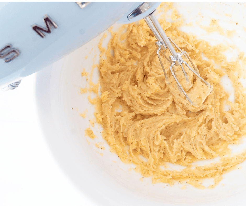 blue hand mixer beating brown butter and sugar in a white bowl