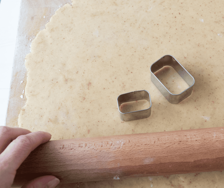 Photo of rolled out dough with a rolling pin with visible rectangular cookies cutters in two separate sizes. 