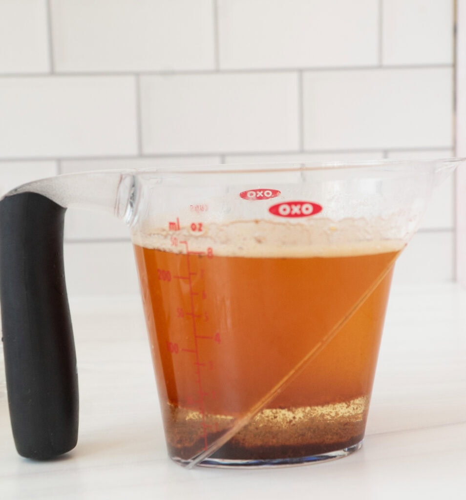 A measuring cup with spout and black handle filled with liquid brown butter. 
