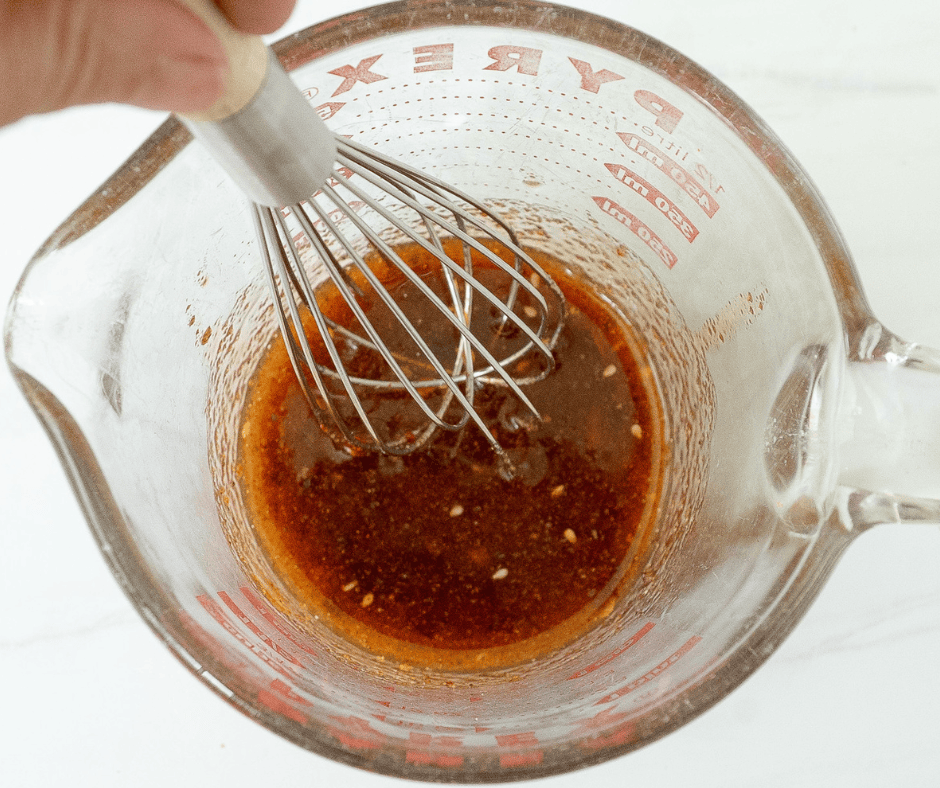 : Two side-by-side process photos: the left shows a hand whisking a red chili crisp and gochujang glaze in a glass measuring cup; the right shows a hand breaking large sourdough pretzels into a glass bowl.
