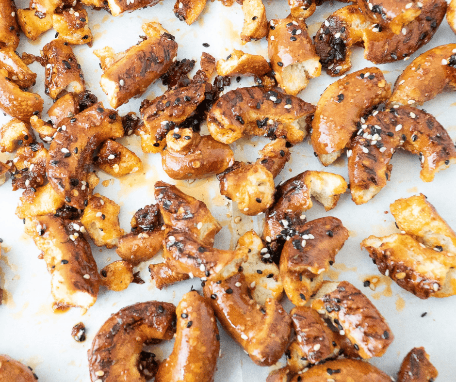An overhead view of broken sourdough pretzel pieces coated in a vibrant red gochujang and chili crisp glaze, spread out on a parchment-lined baking sheet before baking.