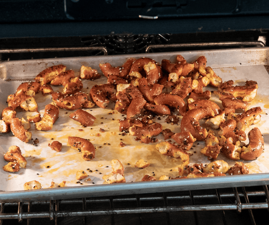 Two side-by-side process photos: the left shows seasoned red pretzels spread out on parchment paper; the right shows the baking sheet inside an oven baking at a low temperature.