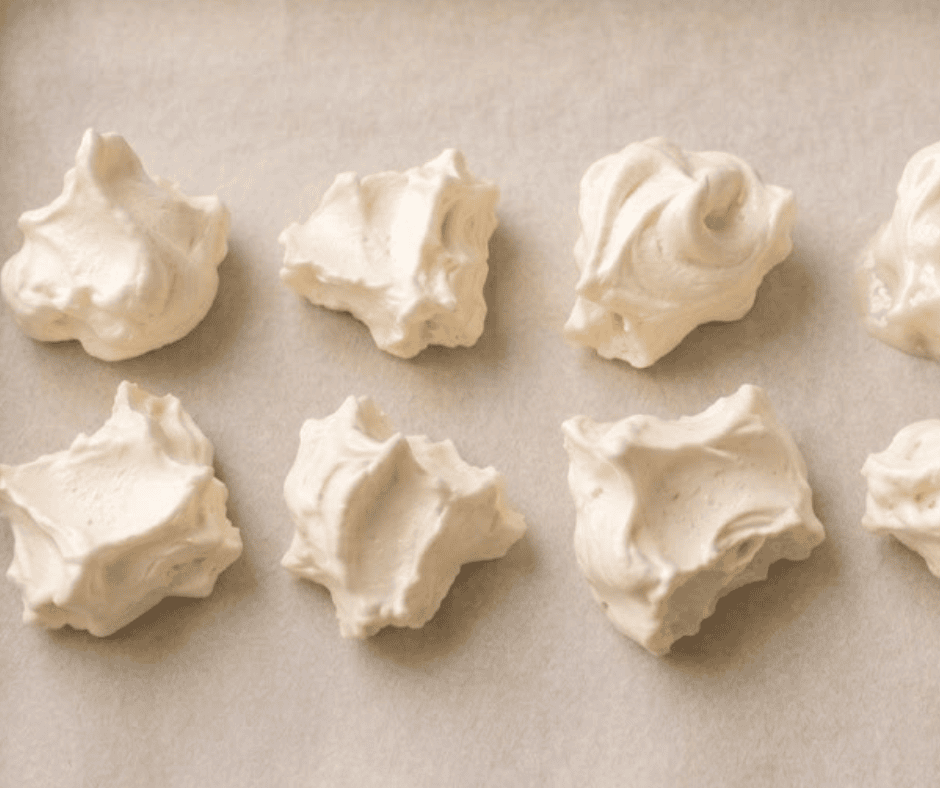 Rustic vanilla-almond meringue clouds shaped with spoons on a parchment-lined baking sheet, ready to bake