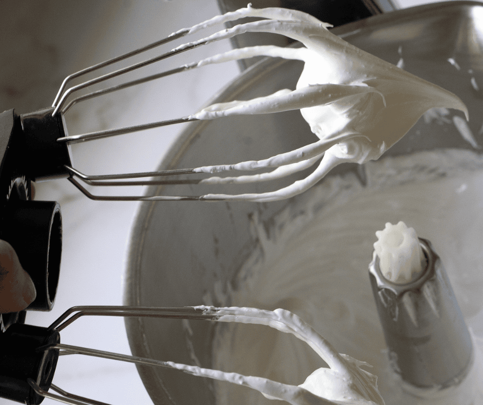 Glossy stiff peaks on the whisk attachment — the meringue is ready when it holds its shape and feels smooth between your fingers