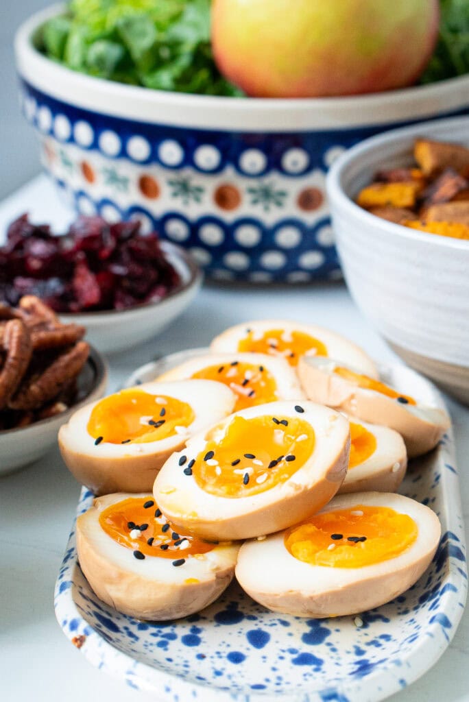 Sliced soy marinated eggs with sesame seeds sprinkled on top with ingredients for the harvest Cobb Salad in the background.